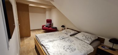 Gesamtansicht des Schlafzimmers, inklusive Doppelbett, Sessel, Schrank und TV