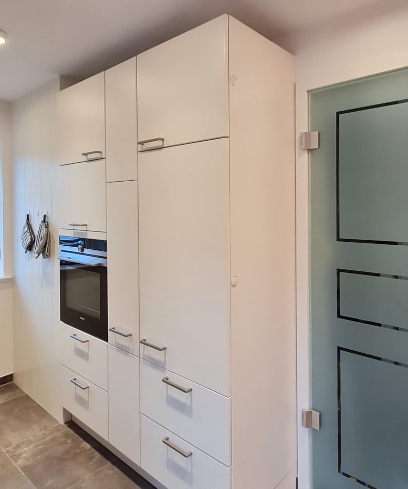 Die rechte Seite der Küche beinhaltet eine helle Schrankwand, mit unterschiedlich großen Schränken und einem eingebauten Ofen